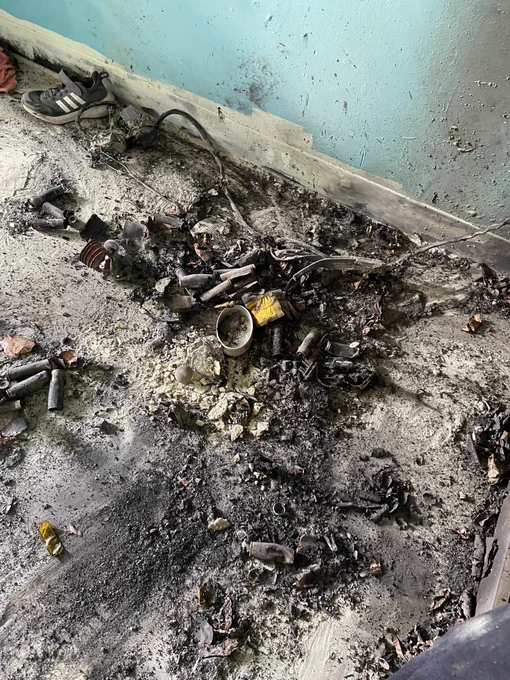 Charred debris scattered across the floor of a unit after a fire, including soot covered floor and walls and smoke damage throughout the room.
