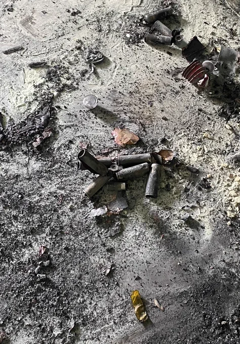 Charred debris scattered across the floor of a unit after a fire, including soot covered floor and walls and smoke damage throughout the room.