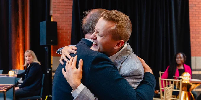 Two people are hugging at an indoor event. 