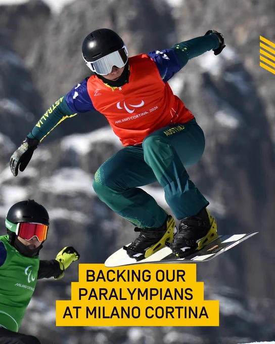 Two snowboarders wearing helmets and goggles are in mid-air on a snowy mountain. Their jerseys have the text "PARALYMPIC GAMES 2026" and "Milano Cortina" with the Paralympic logo. The phrase "BACKING OUR PARALYMPIANS AT MILANO CORTINA" is displayed at the bottom.