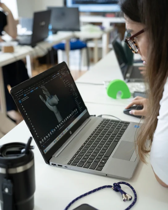 Persona utilizando un ordenador portátil con un software de modelado 3D que muestra una mano en pantalla, mientras maneja un ratón.