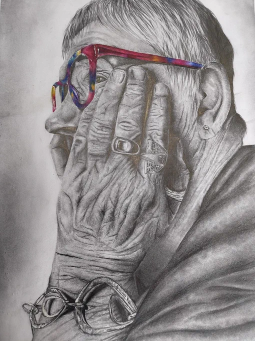 Auntie Val by Anwen from United Sixth Form.
A close-up of an elderly person with colourful glasses resting their face on wrinkled hands adorned with rings and bracelets.