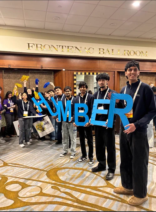 People are holding up cardboard letters to spell out the word Humber.
