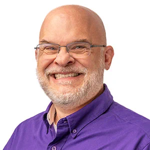 Portrait of man smiling at camera wearing eyeglasses and a purple shirt.