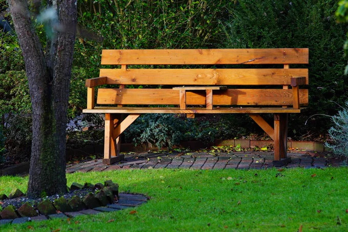 A serene wooden bench in a leafy, sunlit garden perfect for relaxation and solitude.