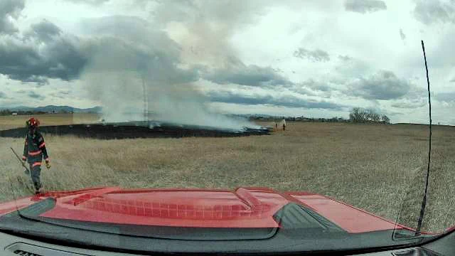 Firefighter walking in a dry field with a burn area and smoke in the background