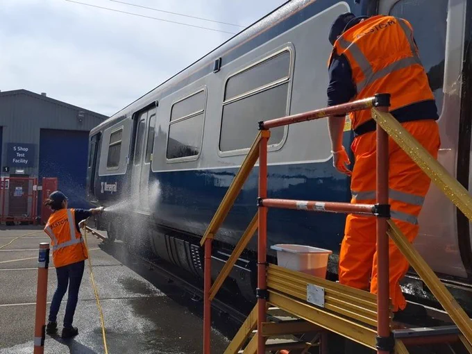Two people in high-vis clothing cleaning the 507 exterior. One is spraying with a hose, the other is working with a bucket and sponge