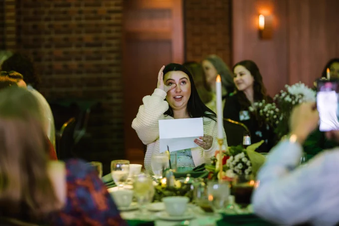 A woman at a dining table wipes a tear while holding a paper, suggesting an emotional moment.\n\n