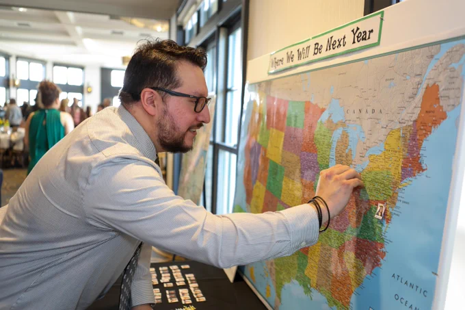 A person places a pin on a large map of the United States labeled \u201CWhere We Will Be Next Year,\u201D marking their residency location during a Match Day event.
