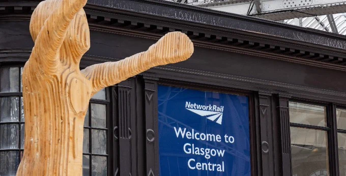 Wooden sculpture in front of a building with a "Network Rail: Welcome to Glasgow Central" sign.