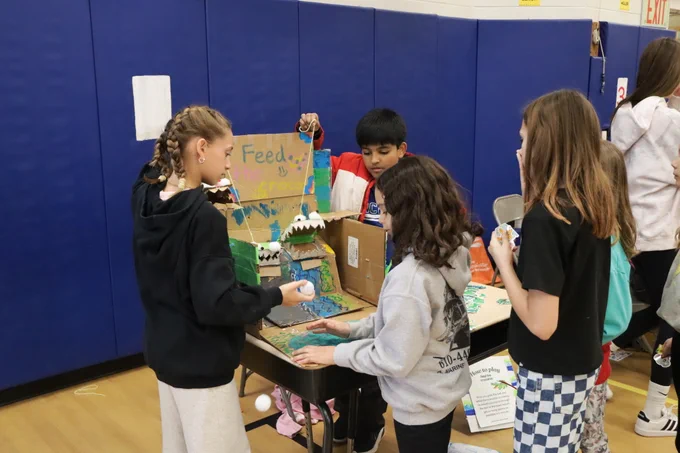 5th graders showing a younger student how to play their arcade game "feed the crocodile"