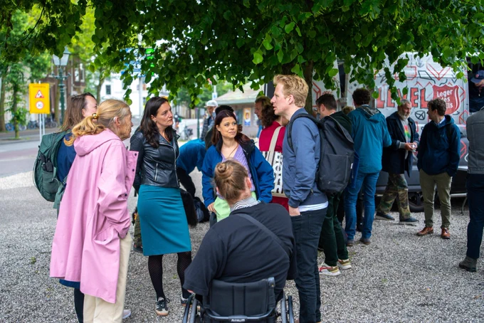 Foto waarop Sandra en ik buiten staan op de Koekamp, met een straatdokter en een grote groep mensen. Daarachter een bus van Level en het Leger des Heils, die ook hulp bieden aan deze groep.
