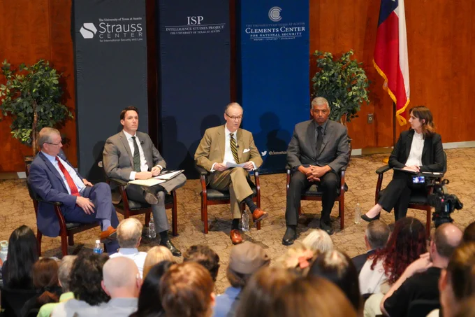 This image shows the five panelists - four men and one woman - sitting in front of the green Strauss Center banner, the dark blue ISP banner, and the mainstream blue Clements Center banner. Taken from an angle behind attendees, the tops of attendees' heads can be seen as the photo focuses on the panelists sitting at the front. 