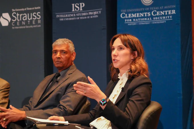 The image shows two panelists -- one older gentleman and one younger woman -- sitting in front of the Strauss, Clements, and ISP banners. The man is looking at the audience. The brown-haired female appears to be speaking to the audience and is gesturing with her left hand as she speaks. 