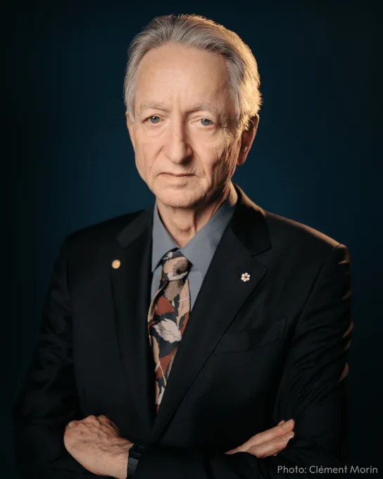 Portrait of Geoffrey Hinton against a dark background, wearing a dark suit with a floral tie. 