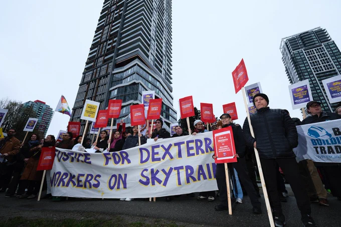 long banner held by group reads justice for dexterra workers on skytrain
