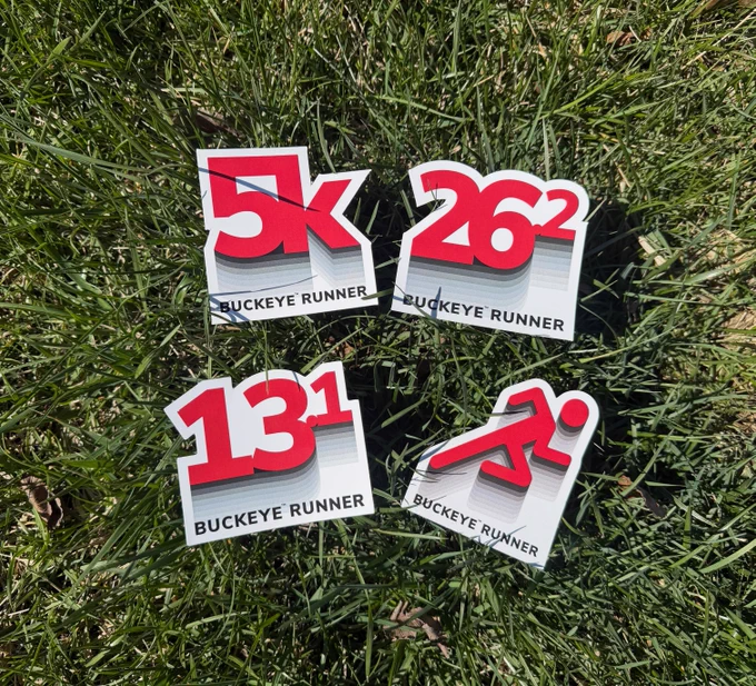 Four stickers displayed on top of grass. The stickers say:
5k Buckeye Runner
26.2 Buckeye Runner
13.1 Buckeye Runner
Buckeye Runner