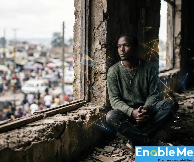 The image shows a young man with dark skin sitting in a window of a concrete building. He is looking out to the left and wearing a dark green sweater. Behind him is a network of glowing yellow and blue lines. In the bottom right corner is a logo for EnableMe with the tagline "Discover your abilities." Underneath the window, out of focus, is a busy street scene.