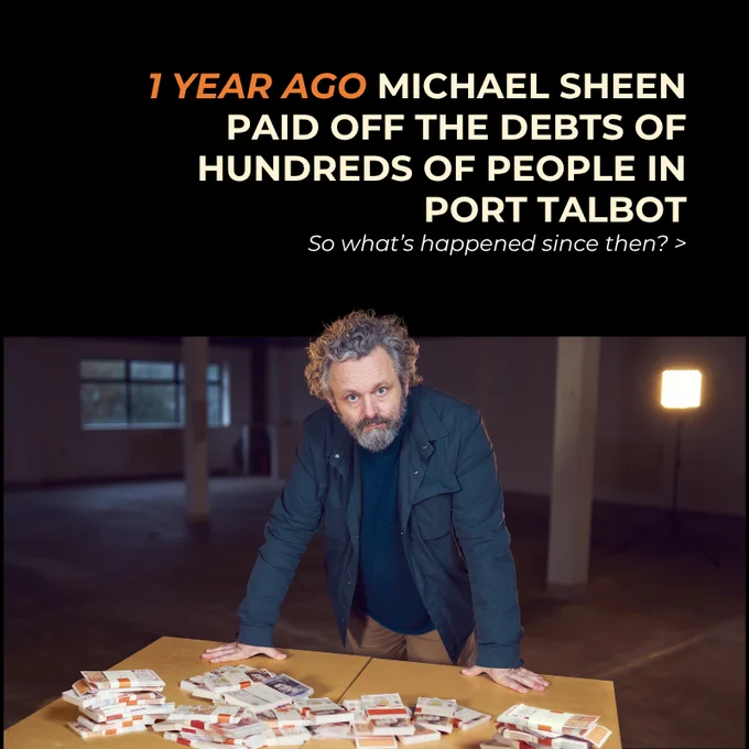 Text says
1 YEAR AGO MICHAEL SHEEN
PAID OFF THE DEBTS OF HUNDREDS OF PEOPLE IN PORT TALBOT
So what’s happened since then? >

A photograph shows Michael Sheen standing, looking at the camera, in front of a tale with piles of bank notes on top of it. 