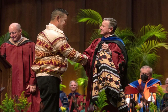 Image of Kyle Doney and FSU President Richard McCullough shaking hands at a commencement ceremony on the stage. FSU Board of Trustees Chairman Peter Collins is on the left side of the image. 