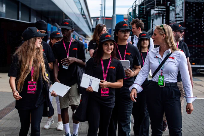 Students attending the Formula 1 Qatar Airways British Grand Prix 2025 walk with a facilitator, wearing Formula 1 caps and lanyards and holding notebooks.
