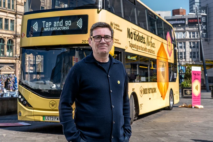 Andy Burnham standing in front of a yellow double-decker bus promoting contactless payment with 'Tap and go' signage.