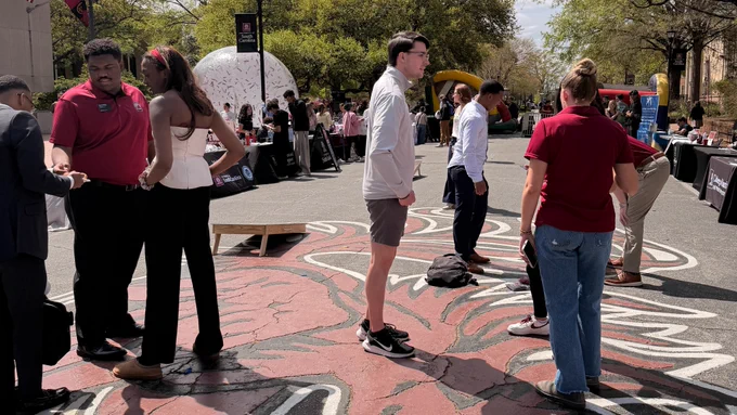 People gathered on a street with a large gamecock bird painted on the pavement during an outdoor event.