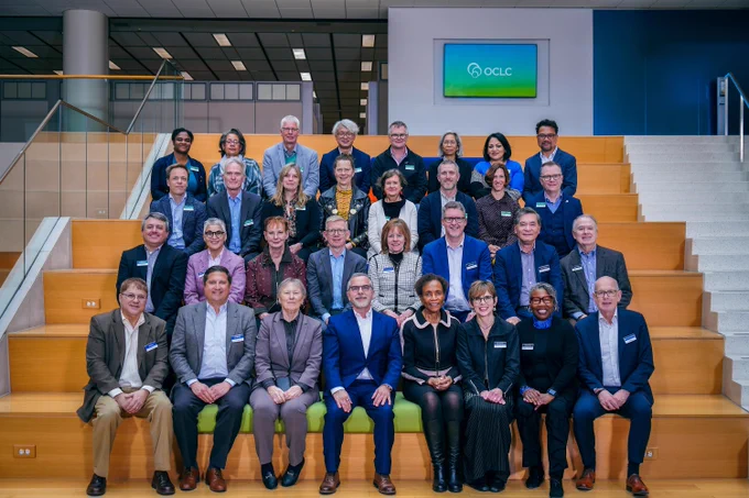 This group photo includes members of the OCLC Leaders Council and OCLC's leadership team. 32 total people are posing on bleacher-style seating in the lobby at OCLC. In the background, the OCLC logo is displayed on a screen.