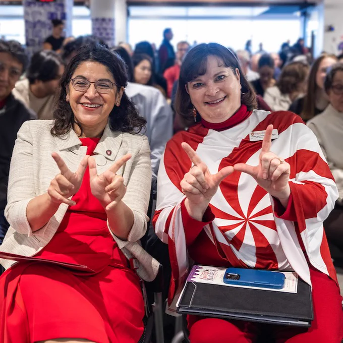 Two women holding their fingers in the shape of a W