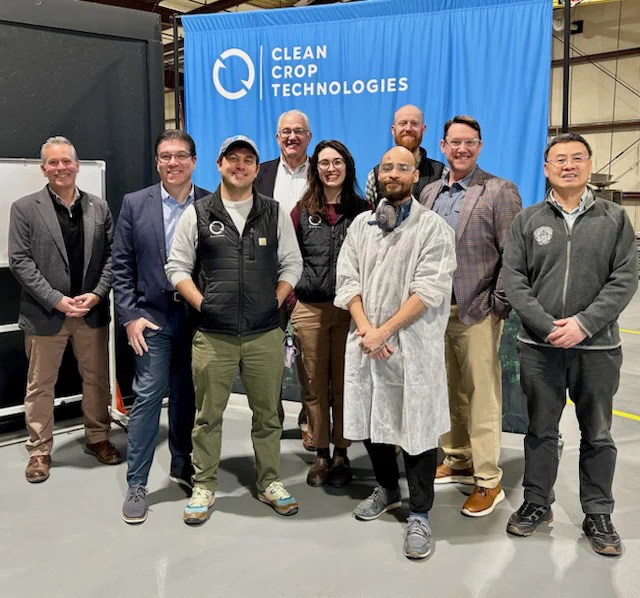 A group of nine people standing and smiling in front of a "Clean Crop Technologies" backdrop.