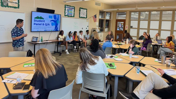 A classroom at Meadow Glen Middle School where a "Student Panel & Q/A" is in progress. A male staff member stands at the front next to a large TV screen displaying the panel title. Five students are seated in a row at the front of the room, facing an audience of adults seated at hexagonal tables. The room is bright, featuring school posters, an American flag, and large windows looking into the hallway.