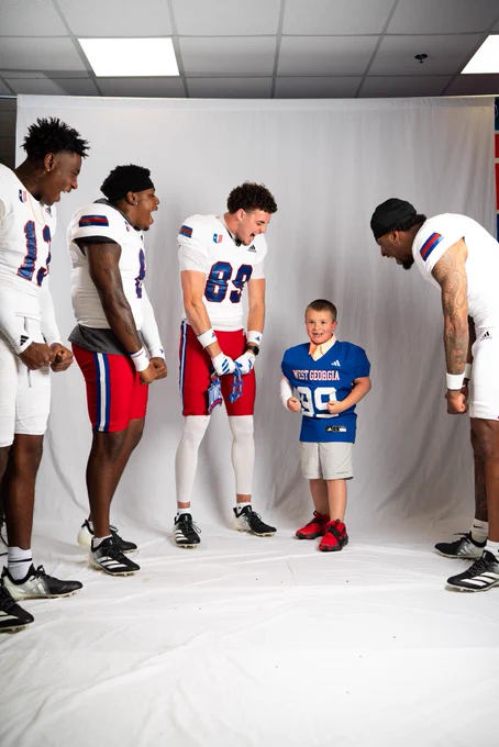 Maddox in a blue West Georgia football jersey posing with four UWG football players in front of a white backdrop