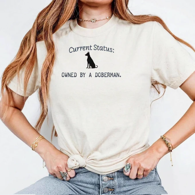 T-shirt for sale that says current status owned by a Doberman. And several colors
