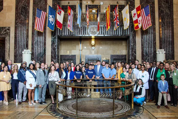 Group of students, faculty, and leaders from Louisiana Community and Technical Colleges gathered inside the Louisiana State Capitol, standing around a circular railing beneath flags.