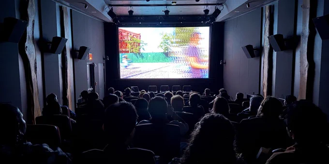 Audience seated in a dark theater watching a bright movie screen with an outdoor scene.