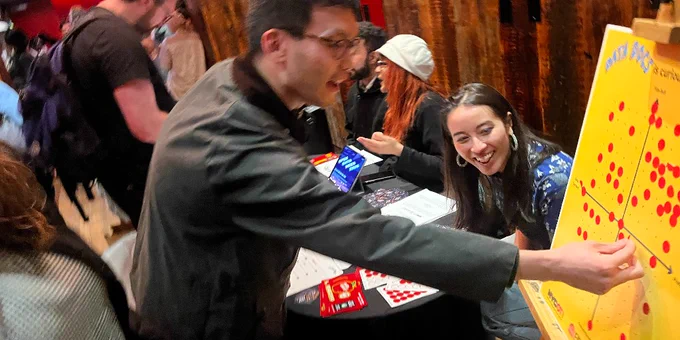 Person placing a red dot on a large yellow board covered with multiple red dots at a busy indoor event for open data documentaries
