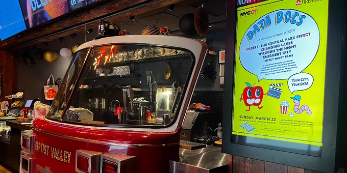 Red vintage fire truck cab converted into a bar setup inside a dimly lit venue with neon signs above and poster for open data week documentaries
