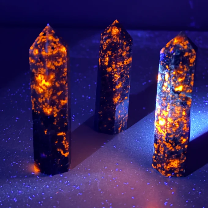 Three dark Yooperlite crystal towers glowing with vibrant orange and yellow fluorescence under a UV light.