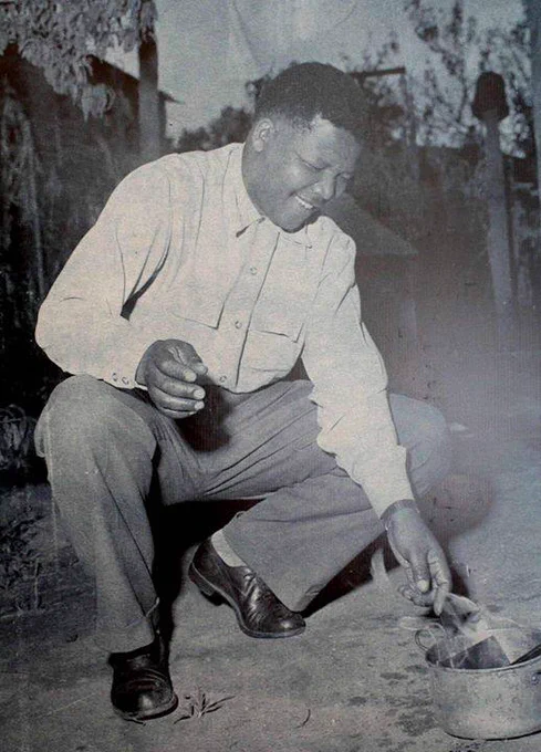 Nelson Mandela kneeling down and smiling as he burns his pass book.