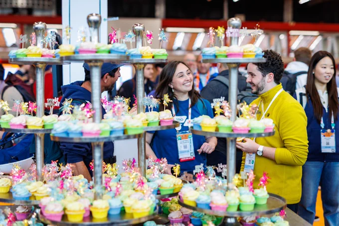 a vibrant display of colorful cupcakes on a multi-tiered stand with Attendees engaging in conversation around the display.