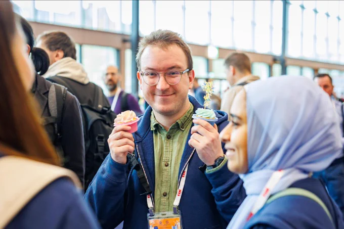 a person wearing glasses and holding cupcakes and smiling