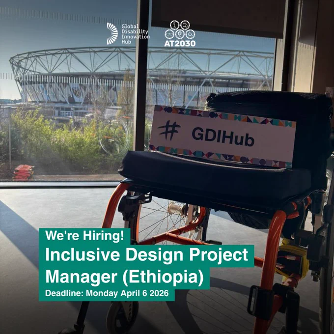 A wheelchair with orange and black frame sits indoors near a large window. A sign reading “#GDIHub” rests on the seat. Outside the window, a stadium structure is visible in the background. At the top of the image are the Global Disability Innovation Hub and AT2030 logos. Text in the lower-left corner reads: “We’re Hiring! Inclusive Design Project Manager (Ethiopia). Deadline: Monday April 6 2026.