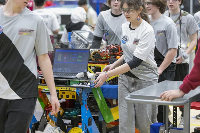 Several people wearing safety glasses are moving a bench filled with electronic equipment.
