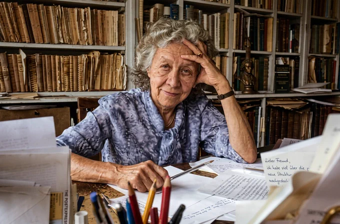 A majestic photograph of a venerable, elderly scholar in her sanctuary of books and manuscripts. The lighting and composition suggest a moment of deep listening, as if the whispers of Thucydides and the chords of Beethoven were present in the air. This image, edited with Photopea, serves as the definitive tribute to Jacqueline de Romilly. It represents the "contactus" between 2026 technology and the eternal heritage of the High Culture.
