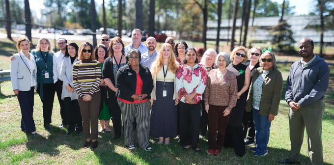 The Statewide IT Procurement Office standing on grass outdoors in a sunny area, with trees and a building visible in the background.