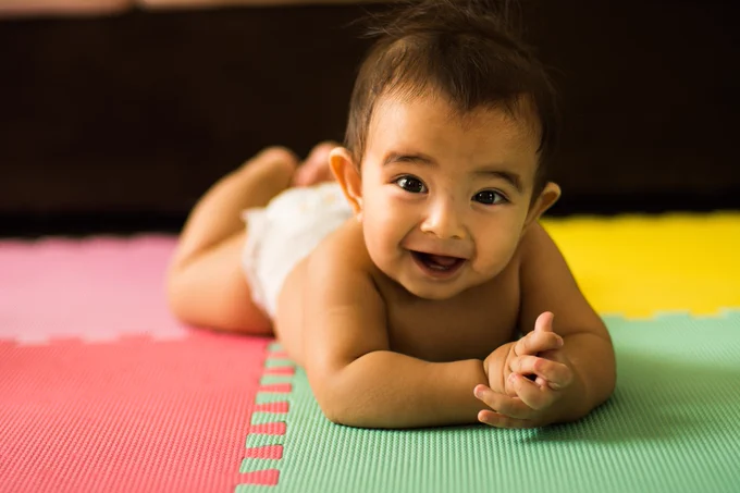 A smiling baby clasping their hands while on their tummy.