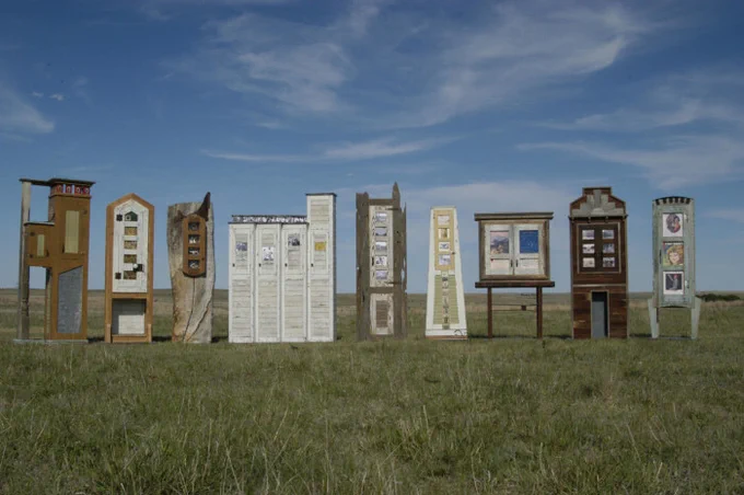 Photograph of the nine pieces from the "Art from the Ruins" exhibit standing out-of-doors on a grassy plain.