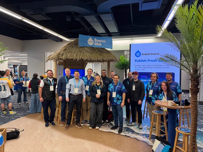 Group of people posing in front of a Source Club booth with a tropical hut and promotional signage at a conference.