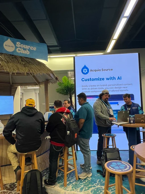 People interacting at an Acquia Source booth featuring AI customization tools and branded content displays.