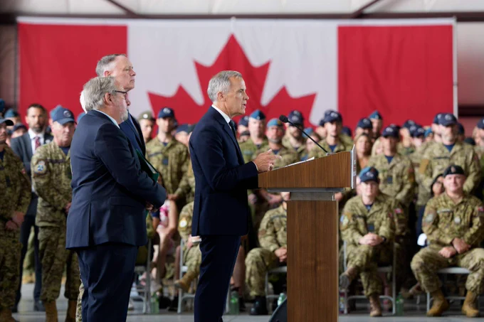 Prime Minister Mark Carney is speaking at a podium before members of the Canadian Armed Forces.